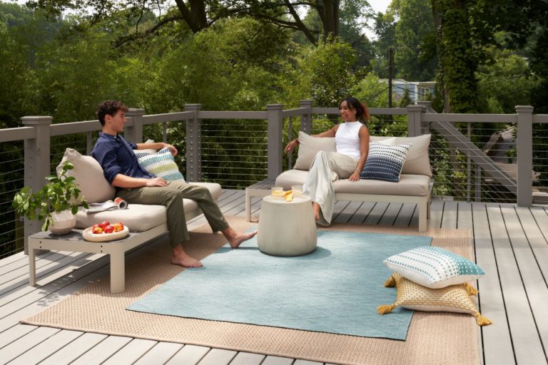 Young man and woman seated on a deck with layered outdoor rugs